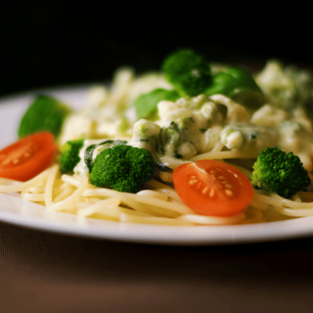 Plate of pasta with cheese sauce, broccoli and tomatoes.