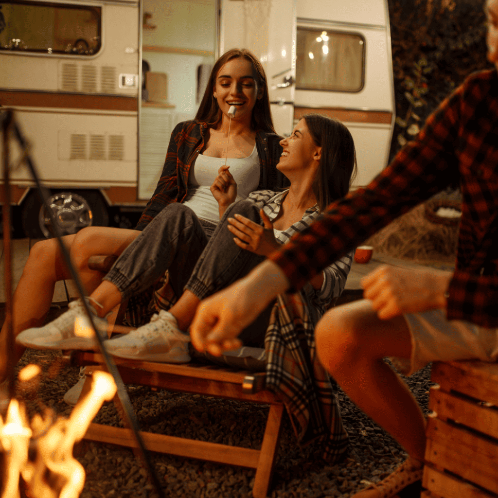 Image of women around campfire in front of an RV enjoying camping.