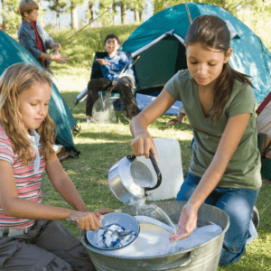 Image of children cleaning dishes in large bucket at a campsite